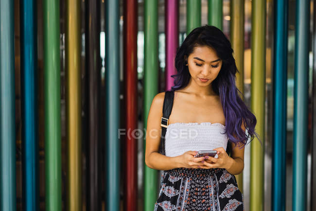 Молодая женщина просматривает смартфон на фоне красочных колонок — стоковое фото