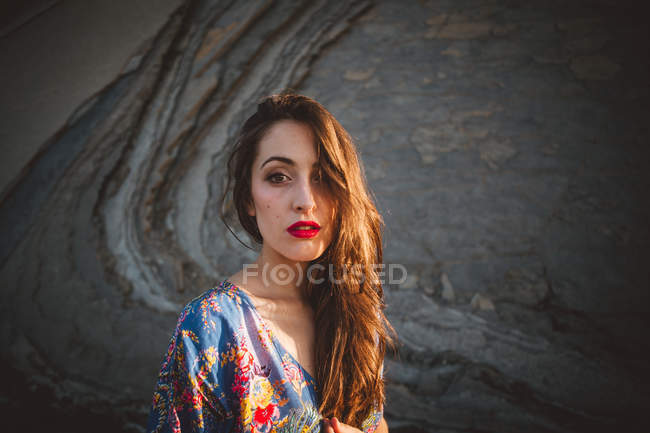 Brunette girl with red lips in dress against rock — Stock Photo