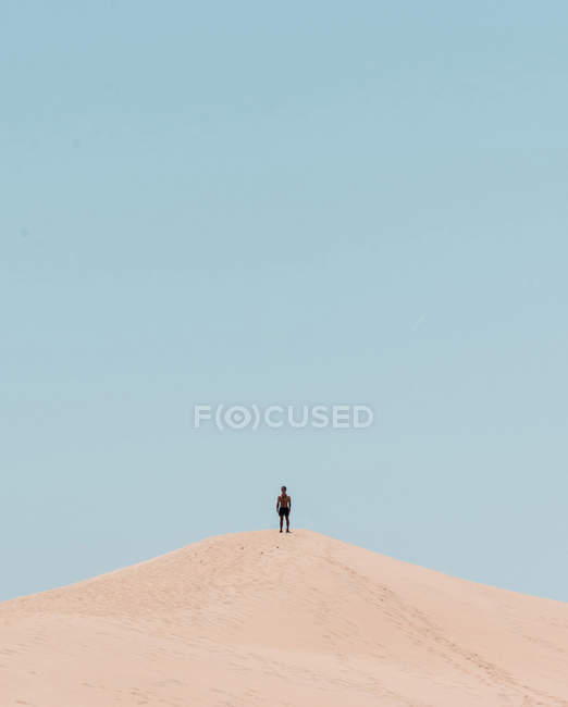 Touriste méconnaissable debout sur une colline sablonneuse dans une journée sans nuages . — Photo de stock