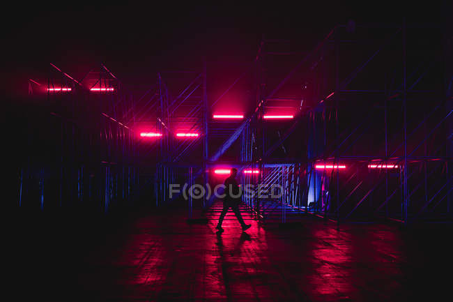 Seitenansicht eines Mannes, der an blauer, nachts rosa beleuchteter Konstruktion wandelt. — Stockfoto