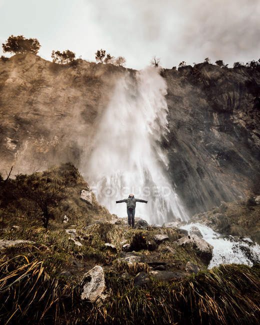 From below view of tourist standing with hands apart at waterfall in nature. — Stock Photo