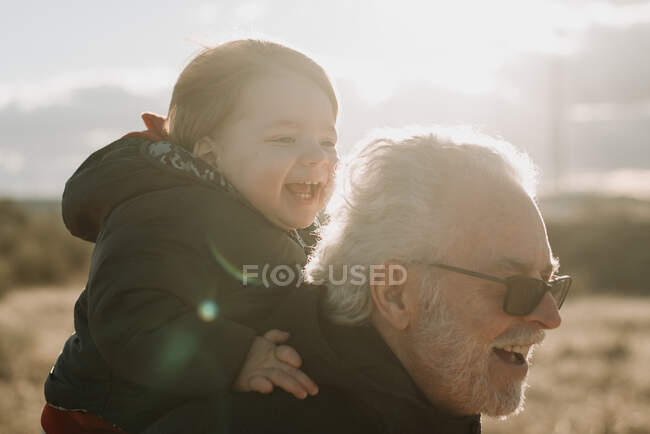 Aged man carrying grandson on back — Stock Photo