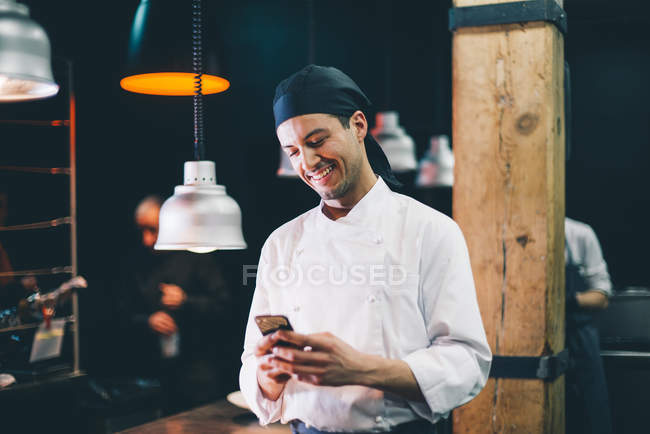 Cheerful chef with smartphone at kitchen — Stock Photo