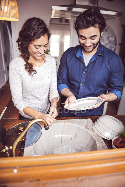 Jovem casal lavar pratos na cozinha — Fotografia de Stock