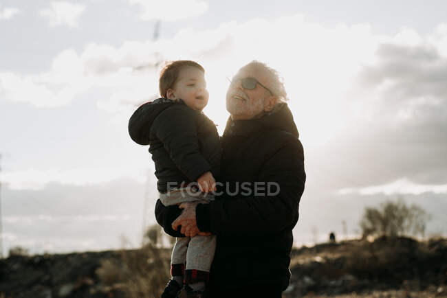 Aged man carrying grandson in arms — Stock Photo