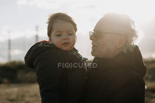 Uomo anziano che porta il nipote in armi — Foto stock