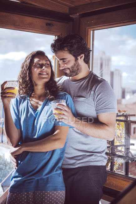 Romantic young couple with juice embracing by window — Stock Photo
