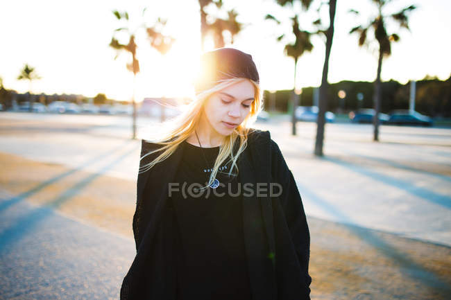 Jovem mulher loira bonita em roupas pretas andando na avenida em dia ensolarado . — Fotografia de Stock