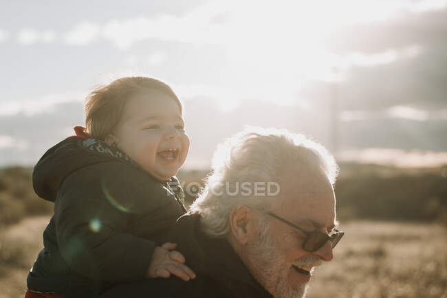 Aged man carrying grandson on back — Stock Photo