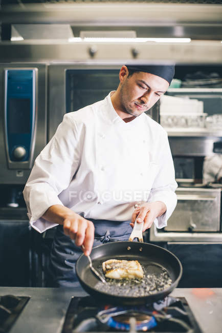 Cook standing on kitchen of restaurant and frying piece of meat on pan. — Stock Photo