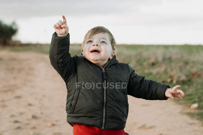 Little boy in coat pointing away looking excited on background of rural fields. — Stock Photo