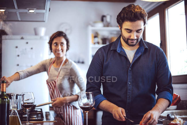 Вид спереди мужчины, режущего ингредиенты на фоне женщины на кухне — стоковое фото