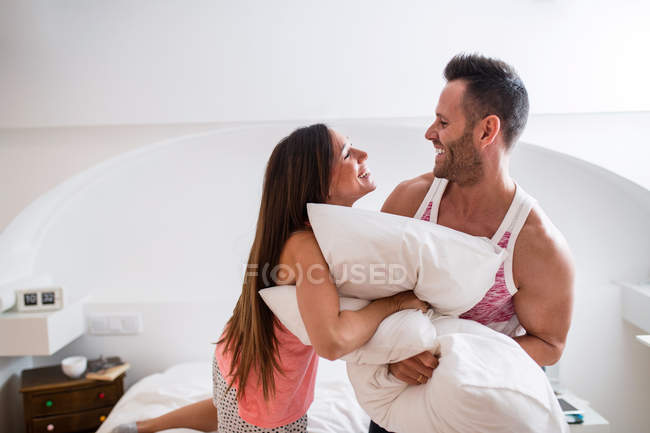 Homem feliz e mulher lutando travesseiros e se divertindo na cama em casa . — Fotografia de Stock