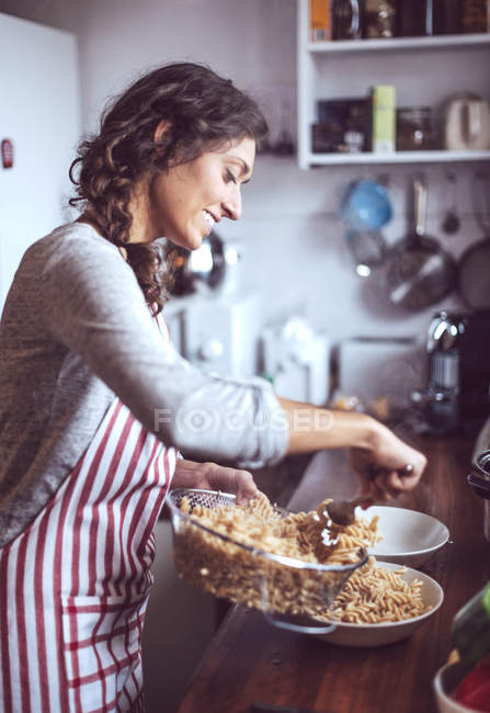 Vue latérale de la femme brune servant des assiettes de pâtes — Photo de stock