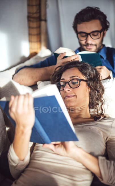 Couple lying on couch at home and reading books — Stock Photo
