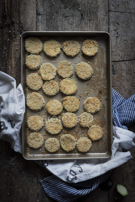 From above shot of zucchini slices in crumbs arranged on sheet pan. — Stock Photo