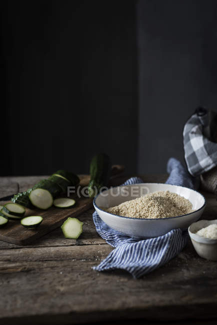 Wooden table with slices of zucchini and bowl of crumbs — Stock Photo
