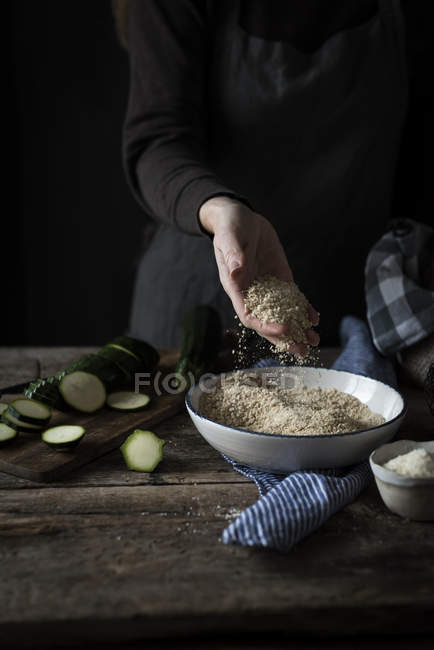 Mão de colheita jogando migalhas de pão na tigela na mesa rústica — Fotografia de Stock