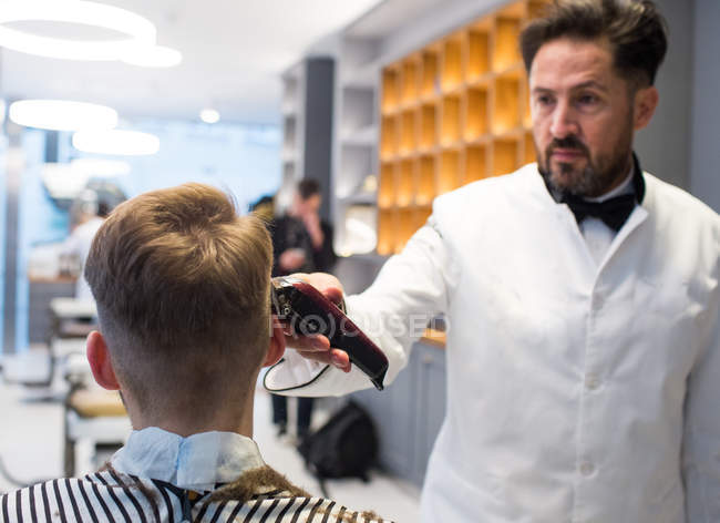 Barber using machine and grooming customer in hairdressing salon. — Stock Photo