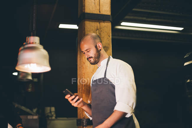 Повар просматривает смартфон на рабочем месте — стоковое фото