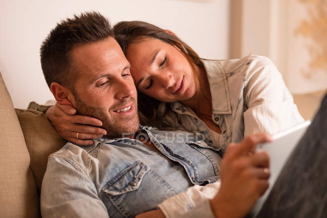 Young loving couple lying together and using tab — Stock Photo