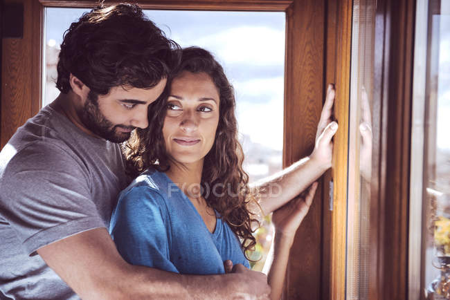 Romantique jeune couple embrassant à la fenêtre — Photo de stock