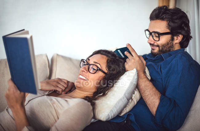 Vista lateral do jovem casal lendo livros no sofá em casa — Fotografia de Stock