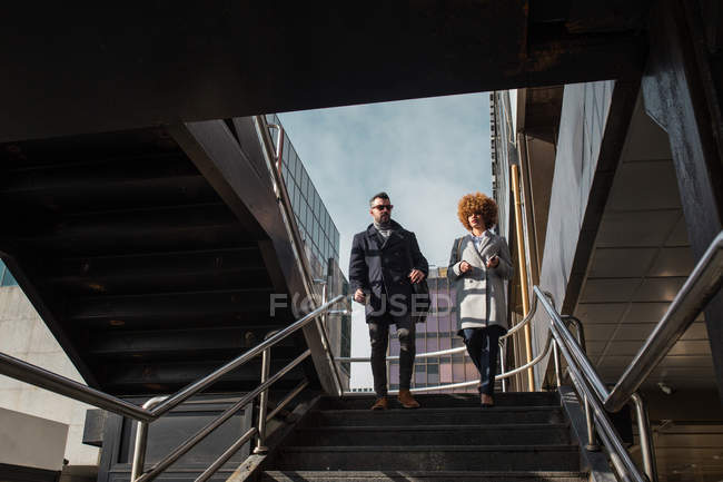 Cheerful stylish couple walking down on stairs — Stock Photo