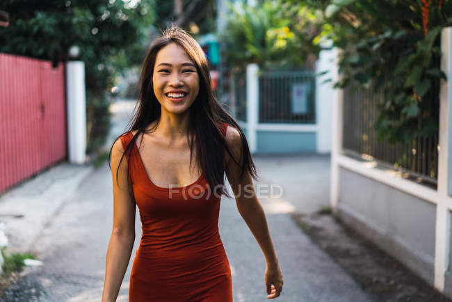 Mujer alegre en vestido rojo caminando por la calle - foto de stock