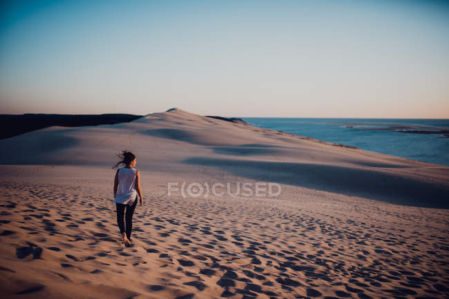 Вид сзади женщины, идущей по песку и оглядывающейся в сторону — стоковое фото