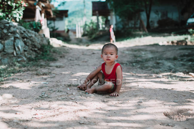 Nong khiaw, laos: entzückender lokaler Junge sitzt auf der Dorfstraße und blickt in die Kamera. — Stockfoto