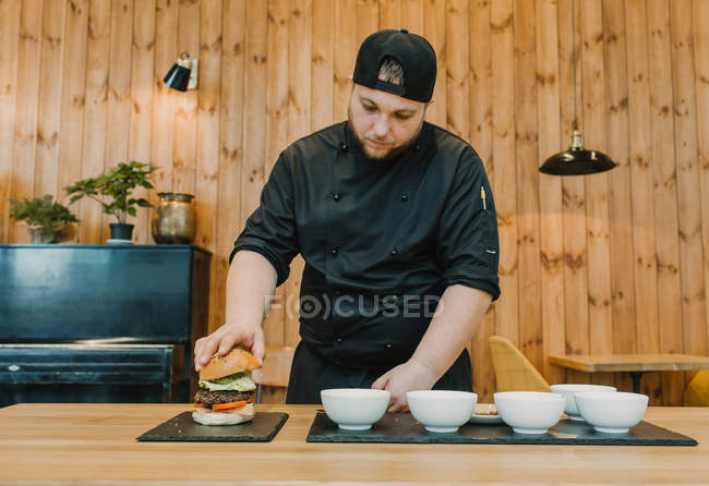 Cook making burger on counter with ceramic bowls — Stock Photo
