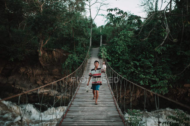 LAOS, 4000 ISLAS ÁREA: Pescador local caminando sobre puente con peces y cañas - foto de stock