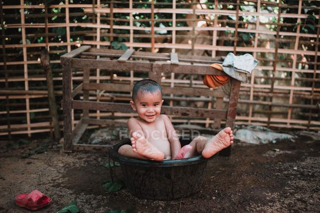NONG KHIAW, LAOS: Smiling child looking at camera while sitting in wash basin. — Stock Photo