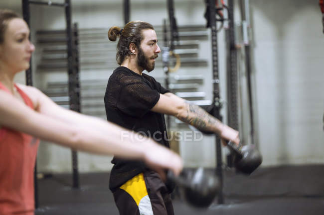 Vista lateral del hombre y la mujer deportistas haciendo ejercicio con pesas en el gimnasio . - foto de stock