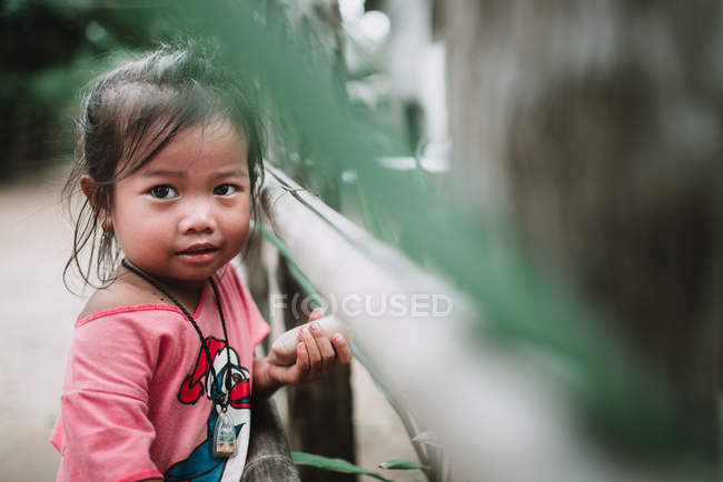 LAOS, 4000 ILHAS ÁREA: Menina em camiseta rosa posando perto de cerca na aldeia . — Fotografia de Stock