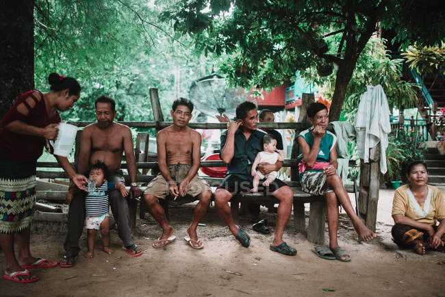 Laos, 4000 Inseln: Gruppe von Einheimischen jeden Alters sitzt auf einer Holzbank im Dorf. — Stockfoto