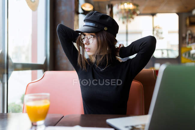 Donna elegante seduta a tavola con succo d'arancia e laptop — Foto stock