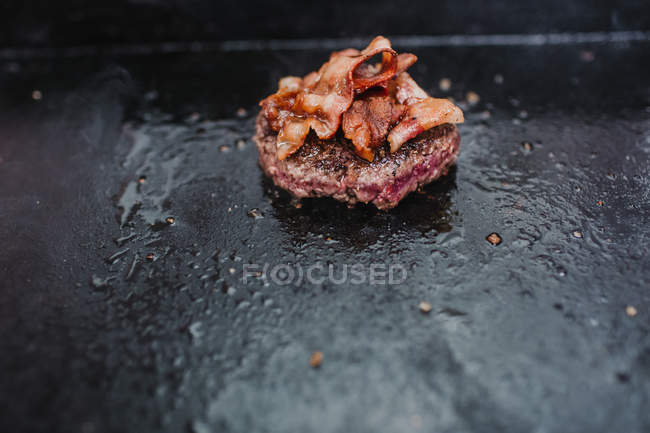 Close up view of patty with bacon frying on stove — Stock Photo