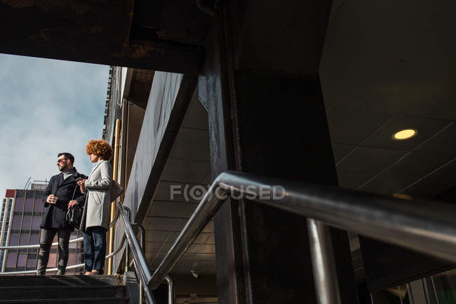Alegre casal elegante em pé nas escadas no dia ensolarado — Fotografia de Stock
