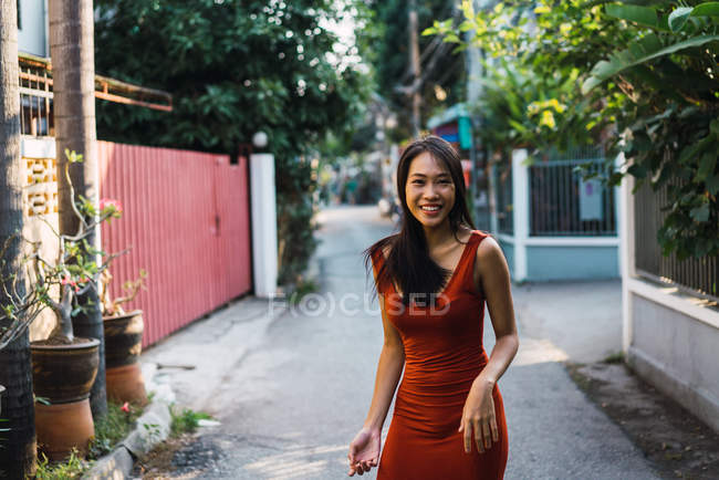 Femme gaie en robe rouge marchant dans la rue — Photo de stock