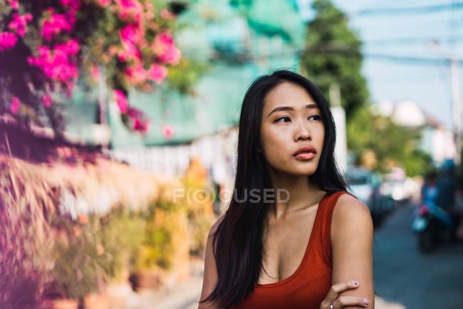 Mujer joven en vestido rojo caminando por la calle y mirando hacia otro lado - foto de stock