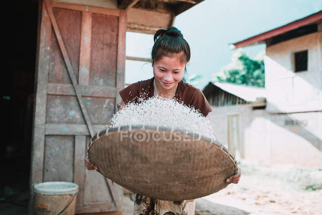 NONG KHIAW, LAOS: Woman winnowing rice in basket while standing on sunny day. — Stock Photo
