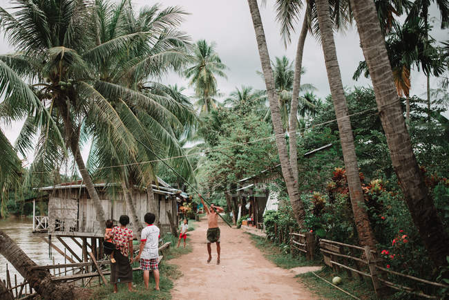 LAOS, 4000 ISLANDS AREA: Street scene of village with man knocking down coconuts. — Stock Photo