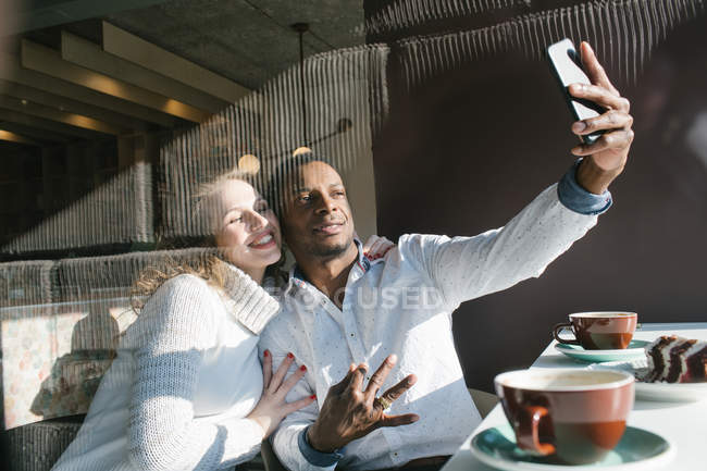 Pareja sonriente tomando selfie con smartphone en la cafetería - foto de stock