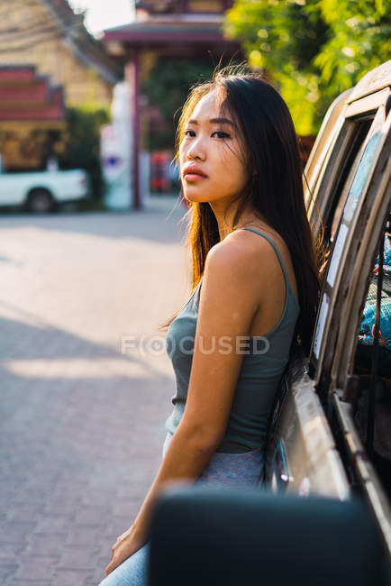 Brunette woman leaning on car and looking away — Stock Photo