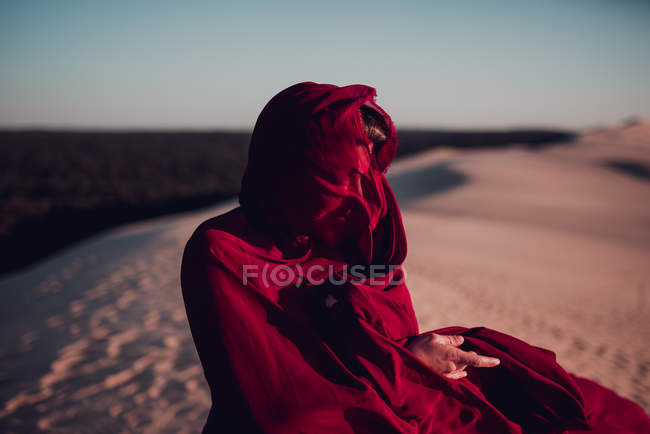 Неузнаваемая женщина, завернутая в красную ткань, стоящая на песчаных дюнах — стоковое фото