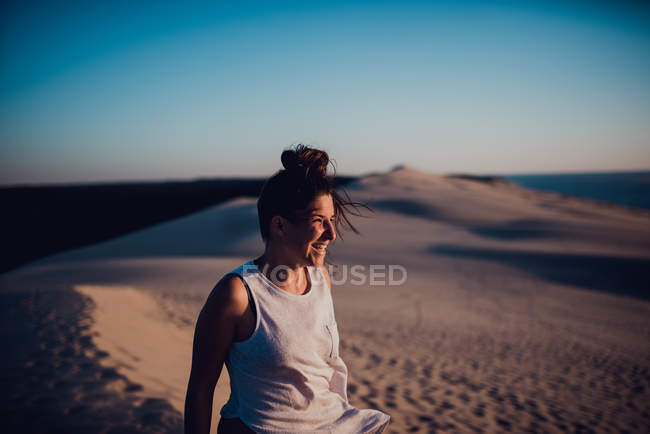 Vista lateral da mulher em pé em dunas de areia e desfrutando do sol . — Fotografia de Stock