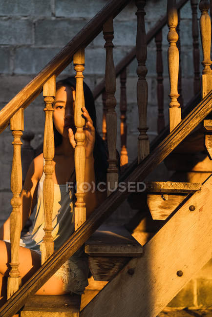 Продумана молода жінка сидить на дерев'яних сходах і дивиться на камеру — стокове фото