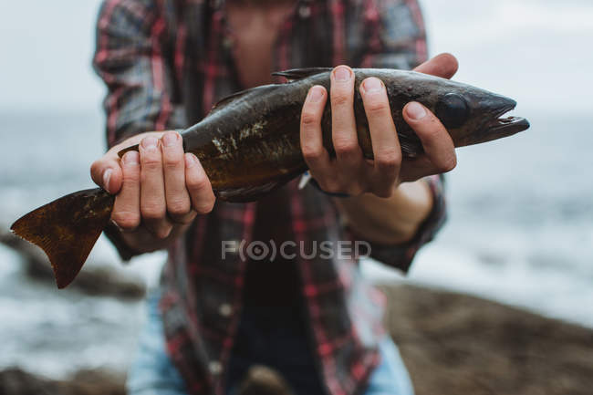 Середина человека держит свежую выловленную рыбу на берегу озера — стоковое фото